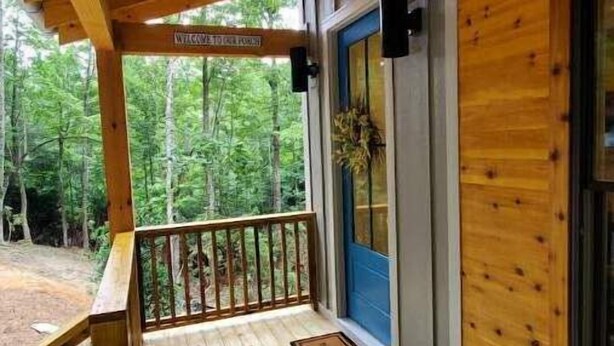 A wooden deck with a railing, a blue door, and a welcome sign. - NEW mountain cottage between Dupont and Pisgah!! (Pisgah Forest)