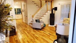 A spacious living area with a wooden floor, a staircase, and a modern fireplace. - NEW mountain cottage between Dupont and Pisgah!! (Pisgah Forest)