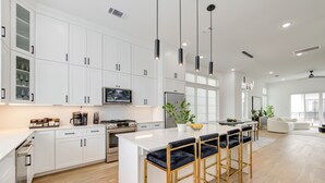 Una cocina moderna con armarios blancos, una isla central con taburetes de bar, horno integrado y un amplio ventanal.