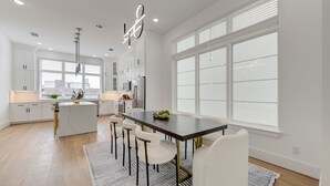 Una cocina moderna con muebles blancos, una isla central y una zona de comedor con una mesa larga y sillas.