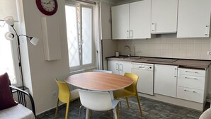 Una cocina compacta con armarios blancos, una mesa redonda de madera y sillas amarillas.