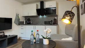 A modern living room with a flat-screen TV, a round coffee table with bottles and a potted orchid, a grey sofa, and a kitchen in the background. - Top Apartment Zentrum Bad Urach 5 Minutes to Train Station (Bad Urach)