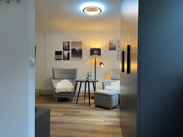 Ett modernt vardagsrum med en grå fåtölj, ett litet runt bord, en golvlampa och en soffa.