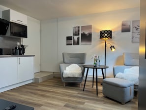 Ett modernt vardagsrum med en grå soffa, ett litet runt bord med drycker, en mikrovågsugn och en lampa.
