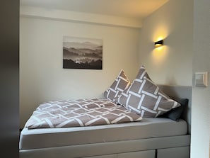 A neatly made bed with patterned bedding, a wall-mounted picture, and a wall sconce.