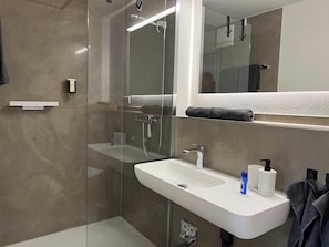 A modern bathroom with a glass-enclosed shower, a white sink with a mirror above it, and a towel rack.