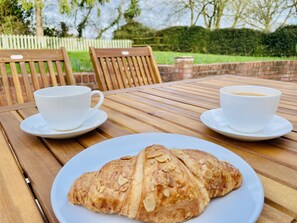 A wooden table with two white cups and saucers, a plate with a pastry, and a brick wall in the background. - Log Burner and Beamed Ceilings-king Size Bed (Worcester)