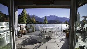 Eine Terrasse mit Tisch, Stühlen, einem Grill und Kübelpflanzen.