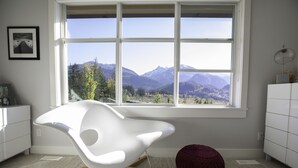Ein moderner Raum mit einem weißen Stuhl, einem roten Pouf und einem großen Fenster mit Blick auf die Berge.