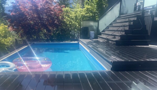 A swimming pool with a wooden deck and stairs leading to a building.