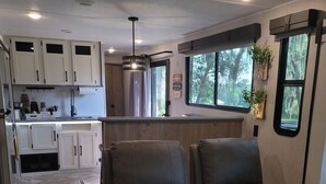Cocina moderna para autocaravana con armarios blancos, una isla central y dos sillones de cuero reclinables.