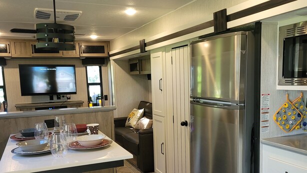 Una cocina moderna con refrigerador de acero inoxidable, televisor de pantalla plana y comedor con mesa dispuesta para dos.
