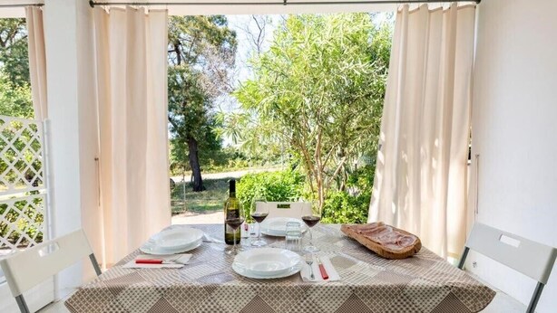 An outdoor dining area with a table set for two, surrounded by white chairs, with a view of greenery and trees. - SuNenneri beach apartment studio 2 (Torre di Bari)