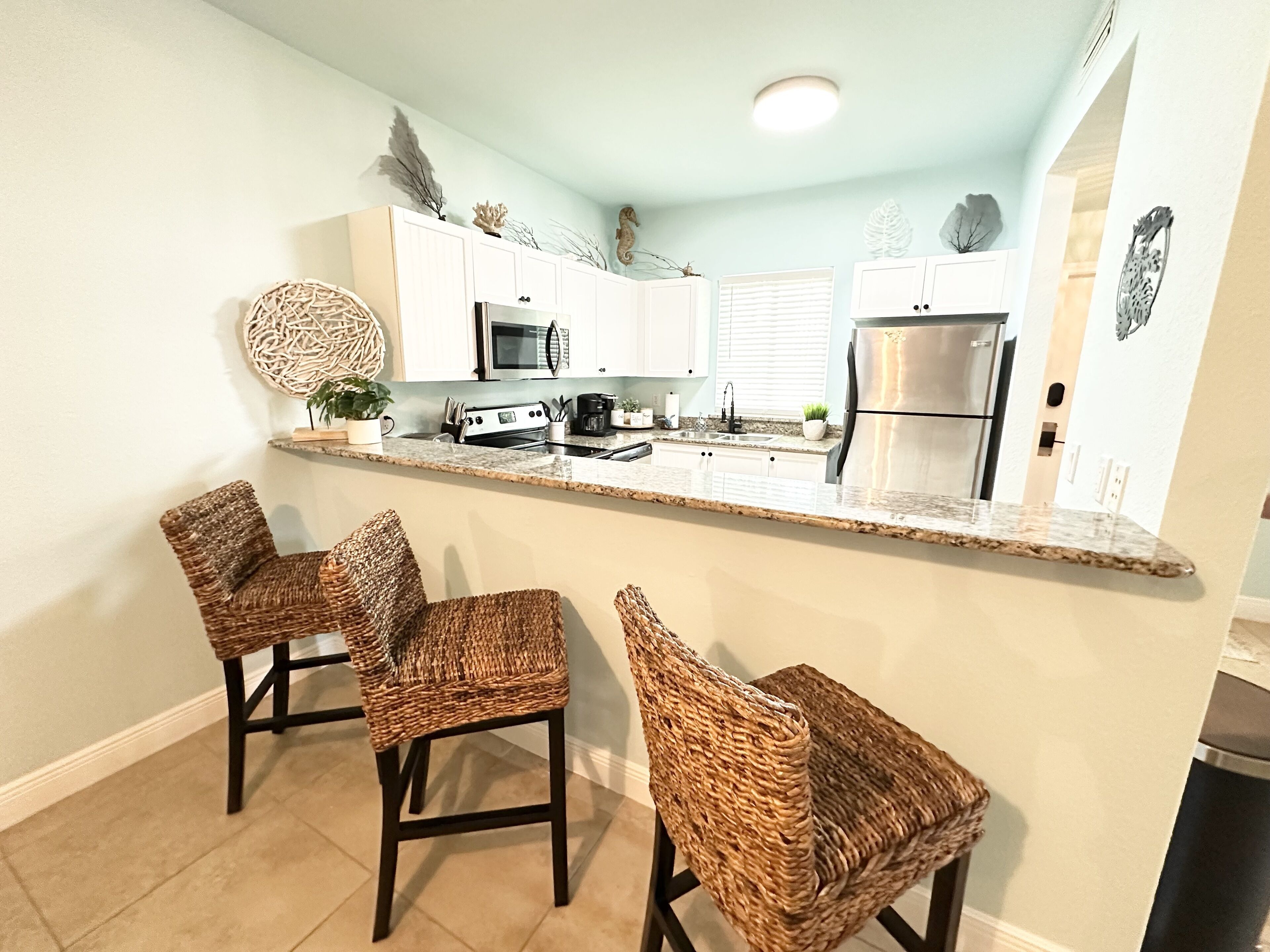 A kitchen with a central island, white cabinets, stainless steel appliances, and wicker chairs.