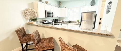 A kitchen with a central island, white cabinets, stainless steel appliances, and wicker chairs.