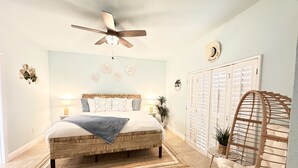 Un dormitorio con cama, lámparas de noche, ventilador de techo, armario y una silla.