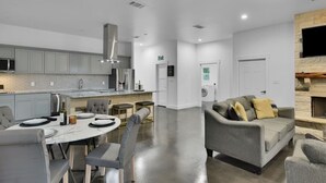 Una cucina moderna con mobili grigi, un'area pranzo con un tavolo rotondo e sedie grigie, e un soggiorno con un divano grigio e cuscini.