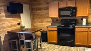 Une cuisine compacte avec des meubles en bois, un four à micro-ondes et une cuisinière. On y trouve un petit coin repas avec des tabourets et une table.