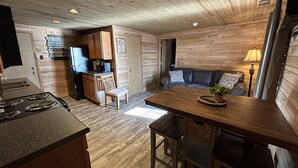 L’intérieur chaleureux d’un chalet comprend une table à manger en bois, un canapé, un coin cuisine avec un poêle et un téléviseur.