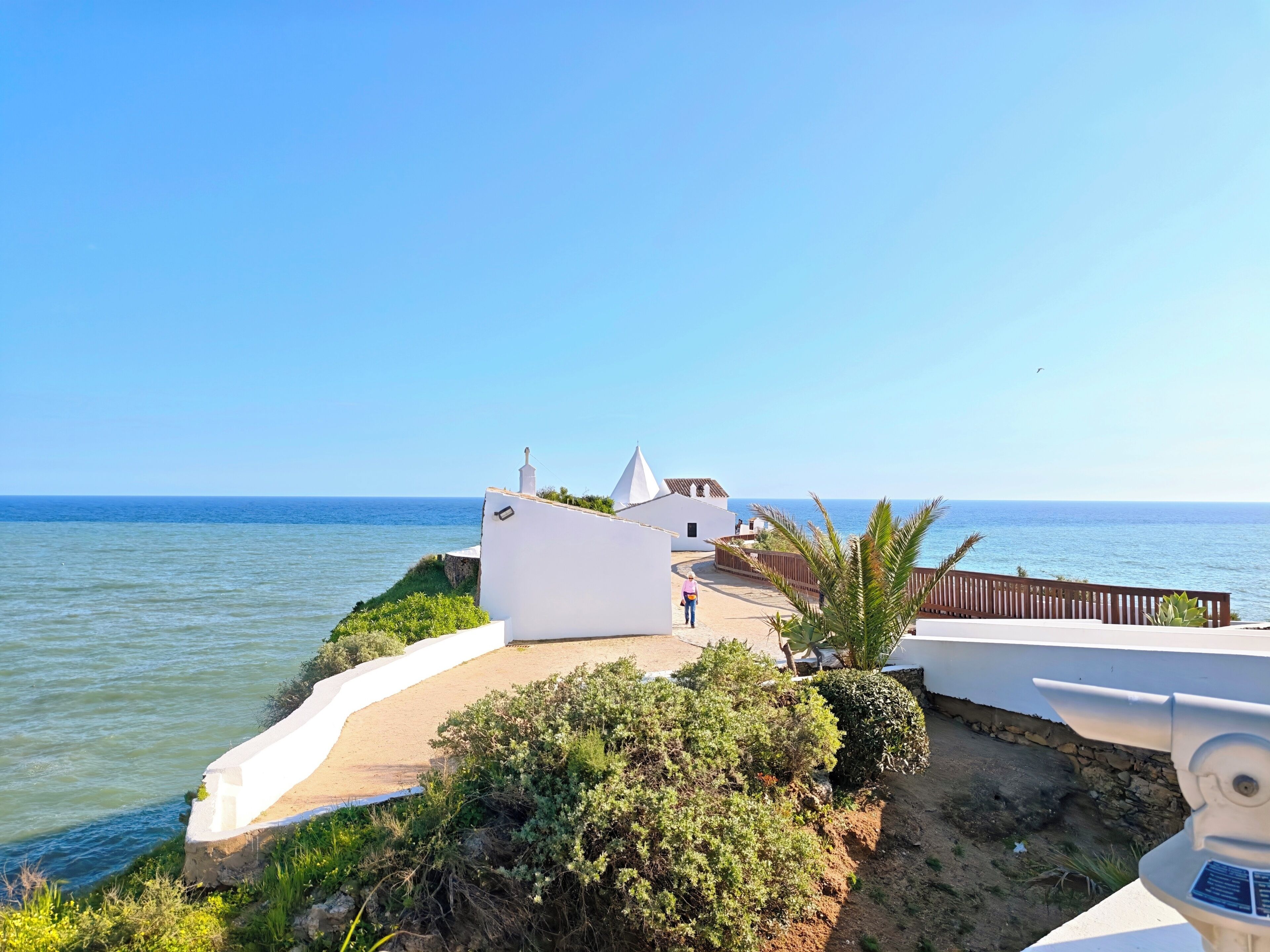 Un bâtiment situé sur la côte, doté d’une façade blanche, d’une promenade dallée et offrant une vue sur la mer.