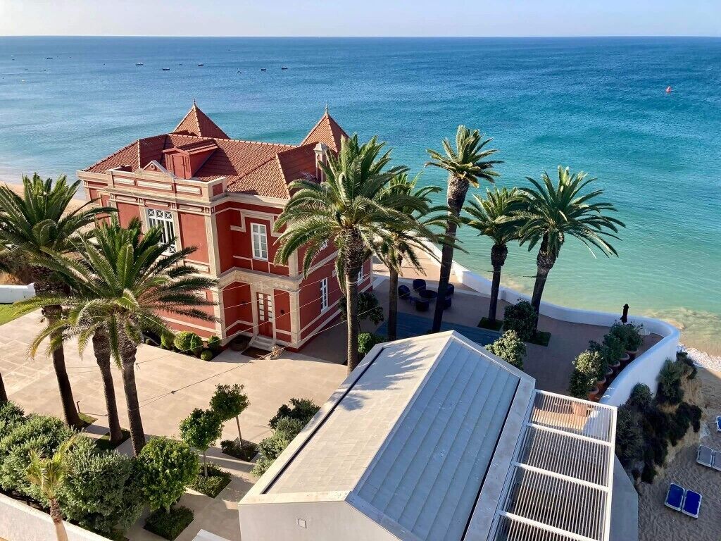 A red building with a tiled roof, surrounded by palm trees and a beach.