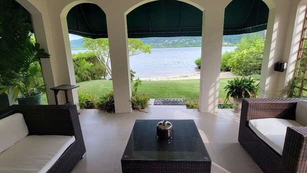 A covered outdoor seating area with wicker furniture and a view of a lake. - The perfect tropical getaway for couples, families and friends! (Montego Bay)