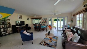 A spacious living room with a blue armchair, a brown leather sofa, a television, and a dining area with a table and chairs. - The perfect tropical getaway for couples, families and friends! (Montego Bay)