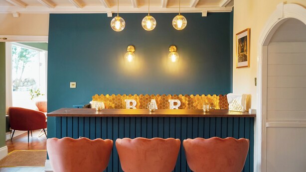 Un espace bar avec trois tabourets de bar roses, un mur bleu et un comptoir de bar orné d’un motif en nid-d’abeilles.