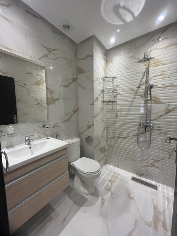 A modern bathroom with a marble backsplash, a glass shower enclosure, a white toilet, and a vanity with a mirror.