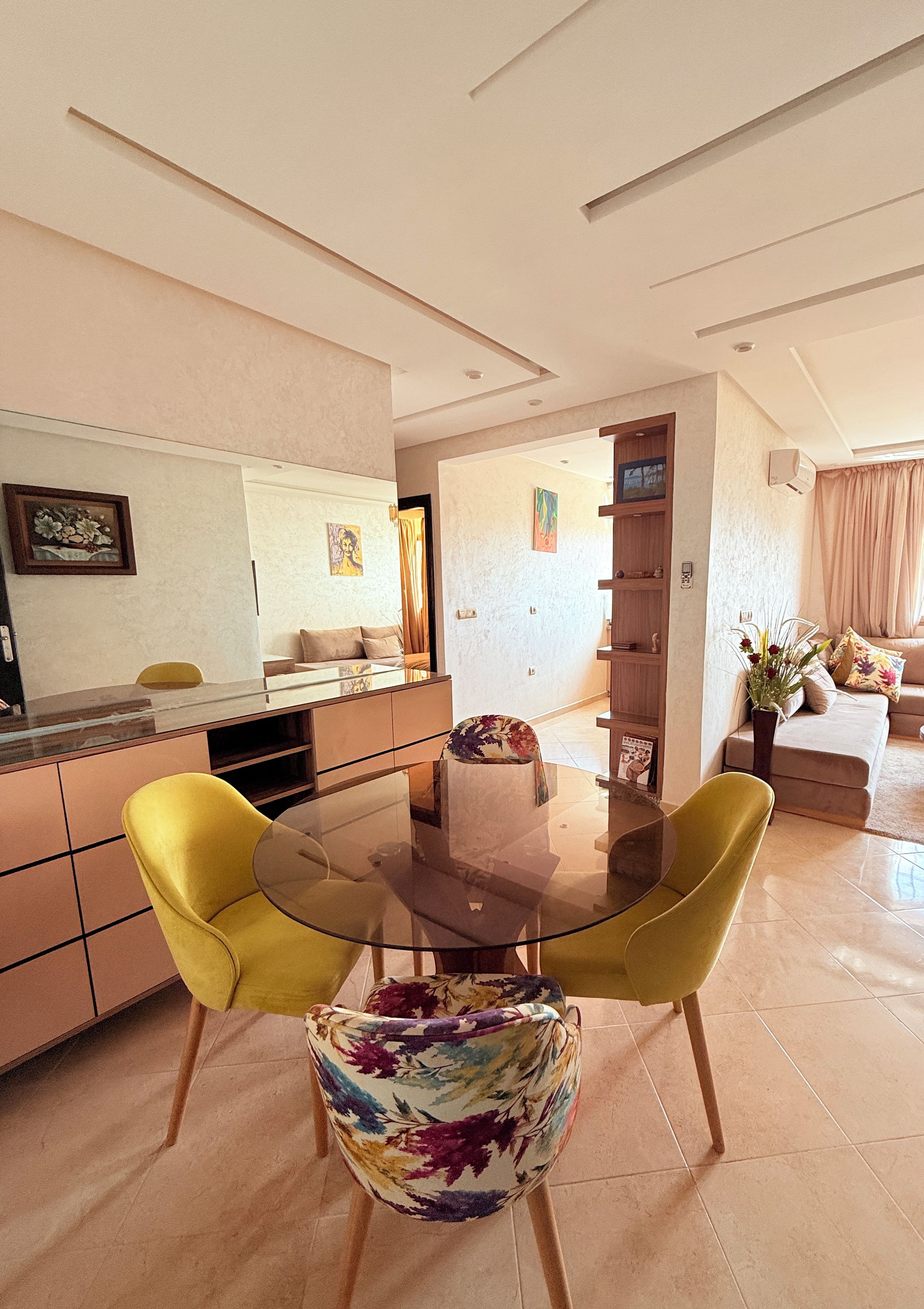 A modern living room with a glass-top dining table, yellow chairs, and a sofa.
