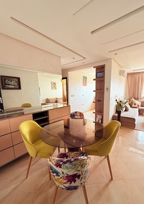 A modern living room with a glass-top dining table, yellow chairs, and a sofa. - restaurant, quiet, family, equipped, air-conditioned, parking, 7 people, agadir (Agadir)