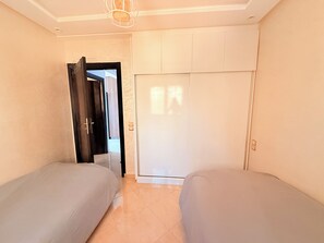 A bedroom with two beds, a wardrobe, and a door leading to another room. - restaurant, quiet, family, equipped, air-conditioned, parking, 7 people, agadir (Agadir)