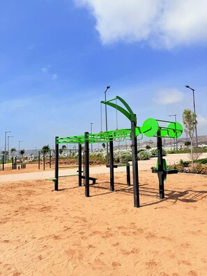 An outdoor exercise structure with a metal frame and green bars, set against a clear sky and sandy ground. - restaurant, quiet, family, equipped, air-conditioned, parking, 7 people, agadir (Agadir)