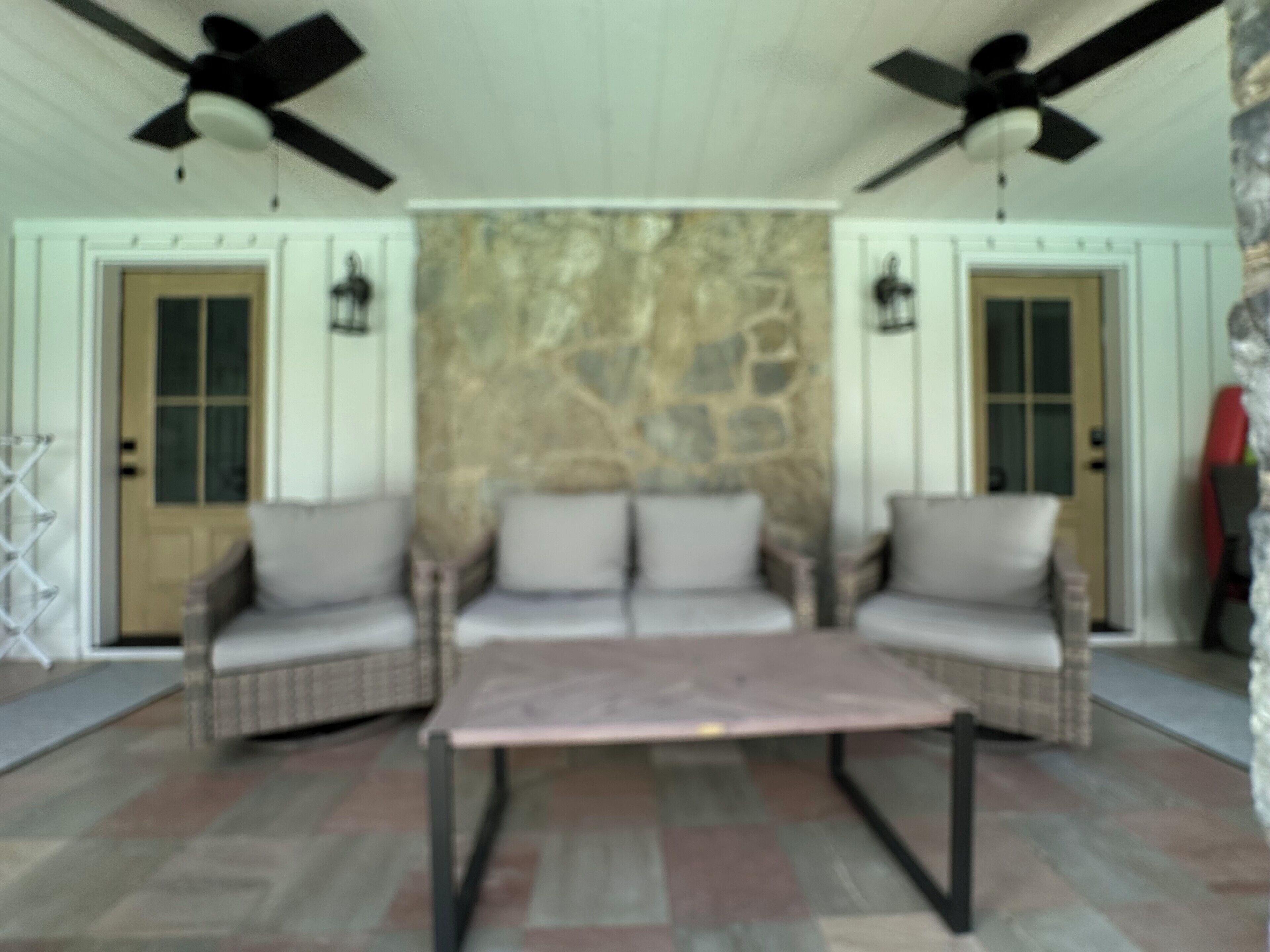 A room with a stone wall, two doors, a ceiling fan, and a seating area with a table.
