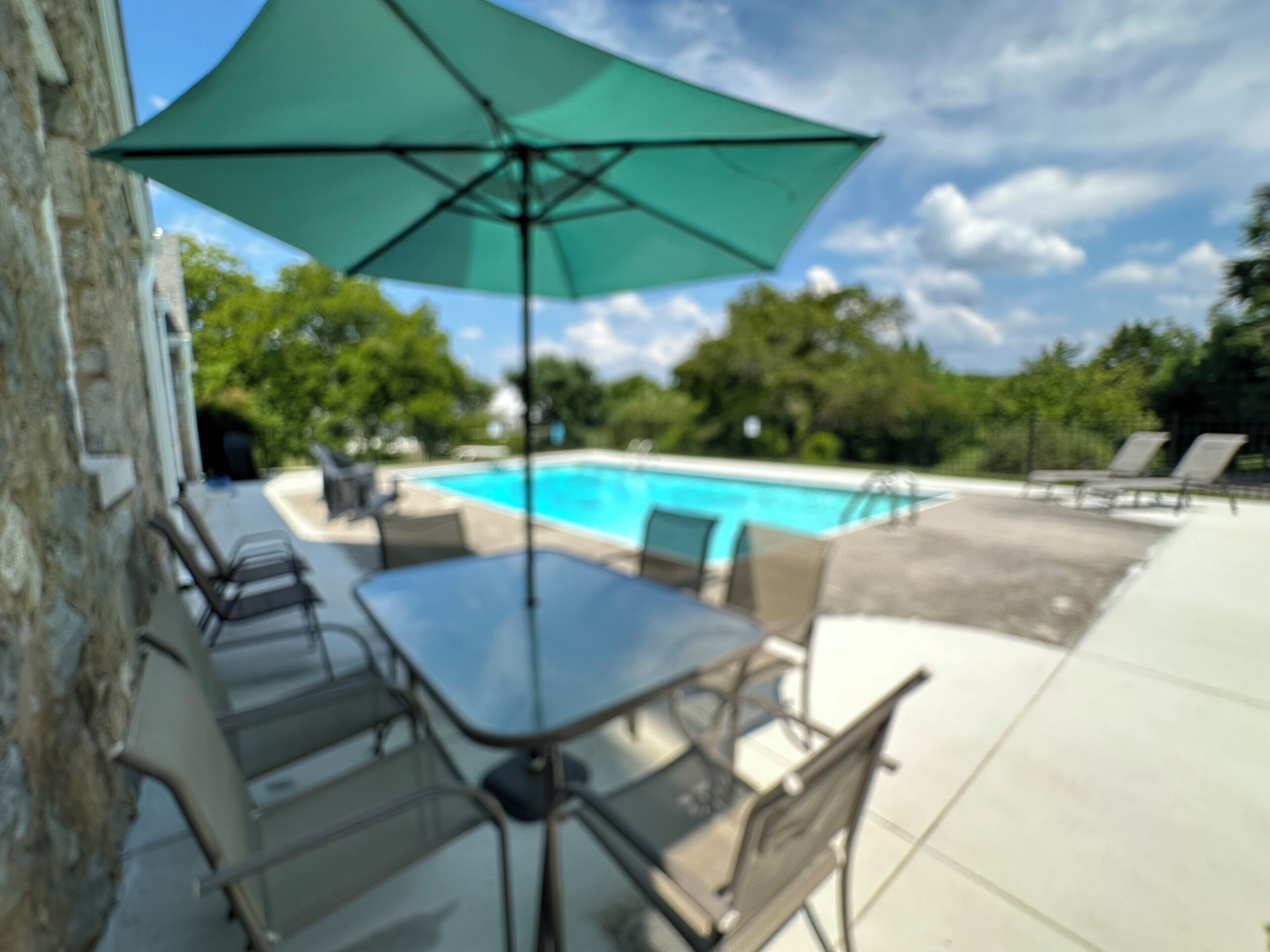 A poolside area with a table and chairs, a large umbrella, and a view of the pool.