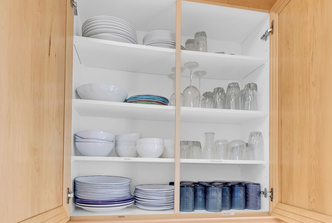 Ein Schrank mit Regalen, der Teller, Schüsseln, Weingläser und Vorratsgläser enthält.
