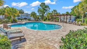 A swimming pool with lounge chairs and a covered seating area, surrounded by palm trees and a brick patio. - Spacious 4 Bedroom, 3 Bath Condo in Pawleys Island: 2-minute drive to pvt beach (Pawleys Island)