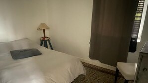 Et hotelværelse med en seng, et lille bord med en lampe, en stol og et mønstret tæppe.