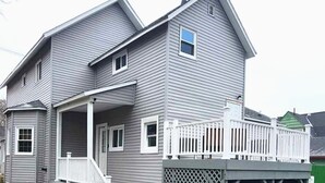 A two-story house with a covered porch and a garage. - Cozy second floor unit in the heart of Downtown Charlevoix, 1BR / 1BA sleeps 4 
 (Charlevoix)