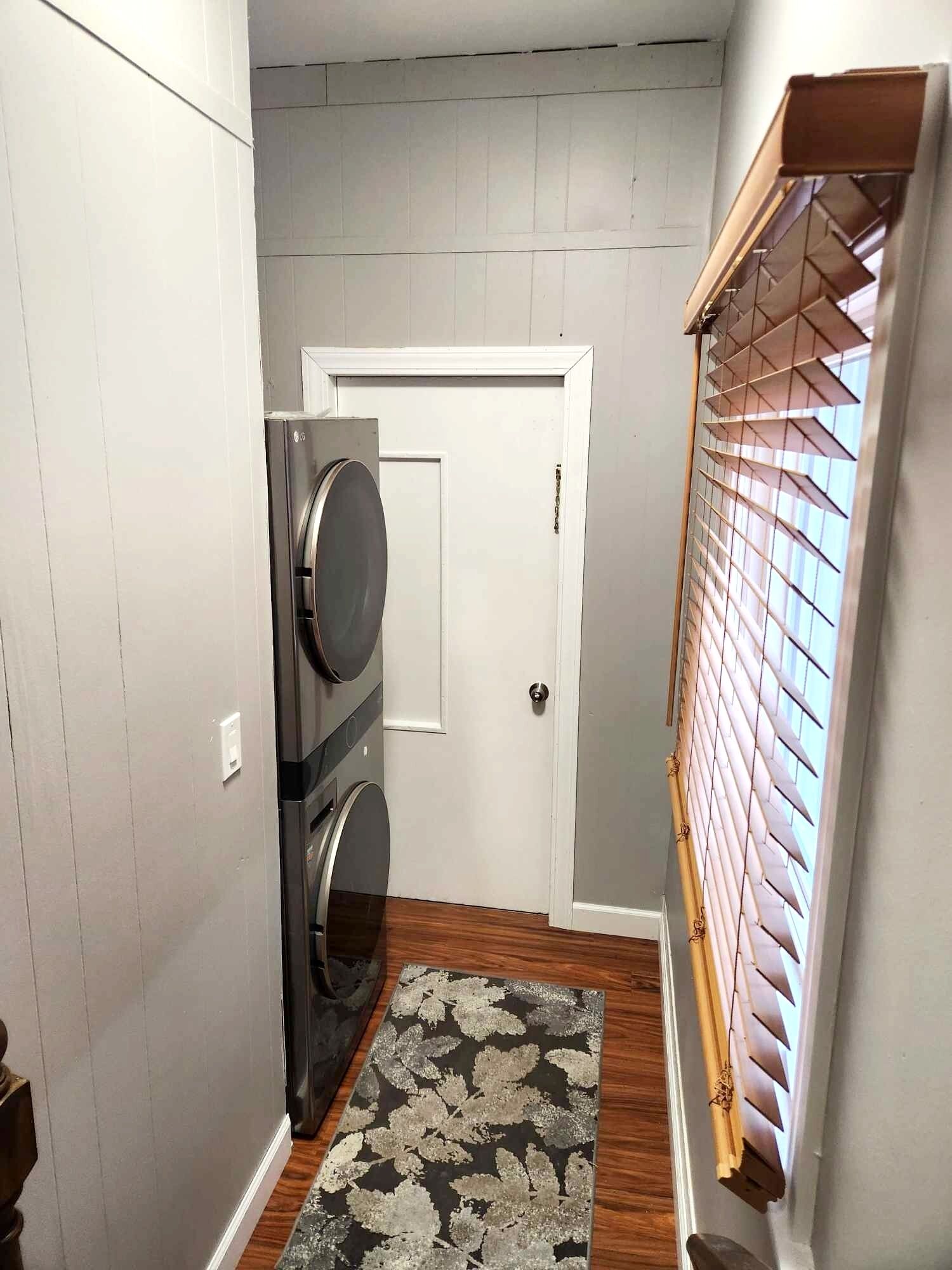 Un lavadero con lavadora, secadora y una puerta con ventana y persianas.