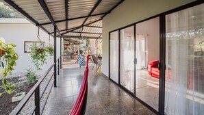 A covered outdoor area with a metal roof, a red hammock, and a red sofa visible through glass doors. - Mini Oasis in Avellanas beach, natural pool, parking, A/C, kitchen #1 (Tamarindo)