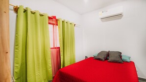 A bedroom with a bed, green curtains, a red bedspread, and an air conditioning unit. - Mini Oasis in Avellanas beach, natural pool, parking, A/C, kitchen #1 (Tamarindo)