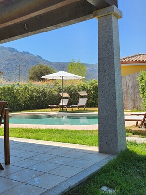 Un patio couvert avec une piscine, des chaises longues et une vue sur les montagnes.