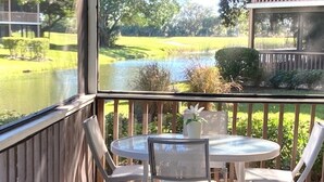 Un patio cubierto con una mesa redonda y cuatro sillas, con vistas a un estanque y un campo de golf.