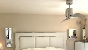 Una cama bien hecha con ropa blanca, una mesita de noche con lámpara y un atril con espejo.