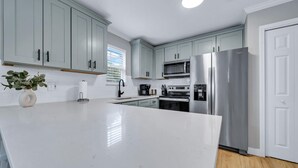 A modern kitchen with light blue cabinets, a white countertop, stainless steel appliances, and a wooden floor. - Highly Rated Cozy 30A Blue Mountain Beach Escape! (Santa Rosa Beach)