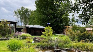 En rustik stuga med en liten damm, omgiven av frodig grönska och blommande växter.