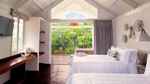 A bedroom with two beds, a TV, a coffee maker, and a balcony with a view of greenery. - Finca San Cayetano (Alotenango)