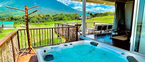 Relax in a hot tub on a shaded deck with a serene view of the surrounding landscape and distant mountains.