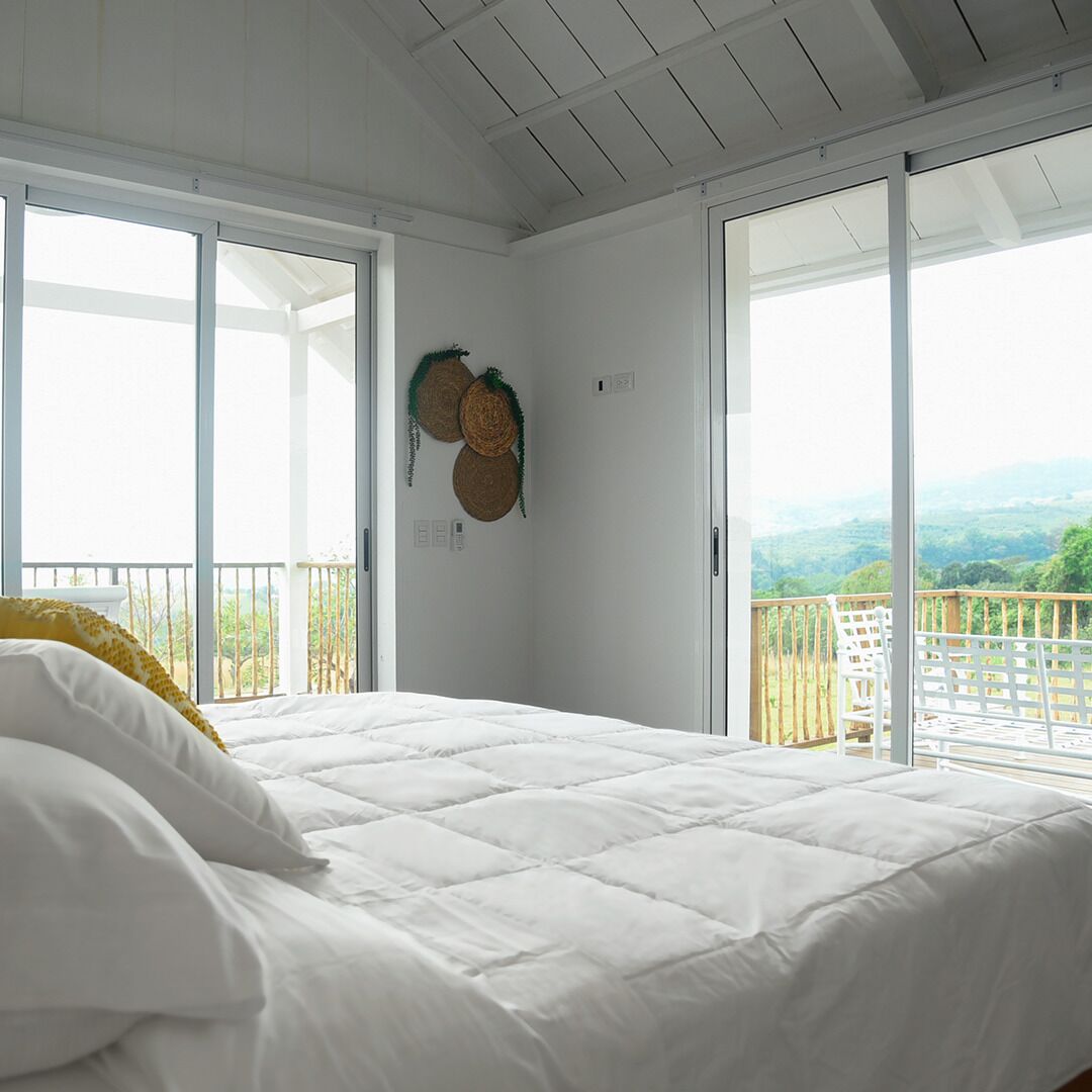 Een slaapkamer met een groot bed, witte muren en een balkon met uitzicht op het landschap.